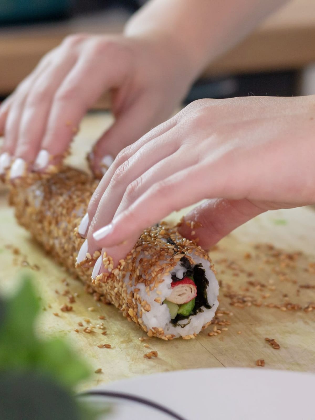 Mãos rolando sushi coberto de gergelim sobre tábua de madeira