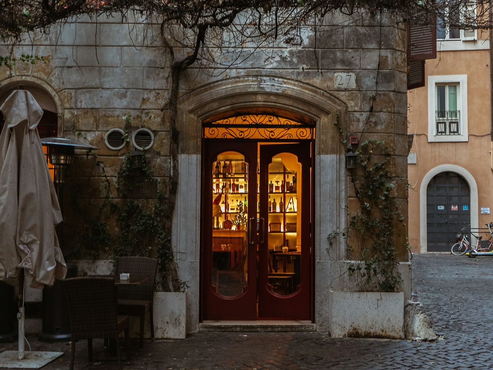 Entrada iluminada de restaurante em fachada de pedra, com calçada de paralelepípedos